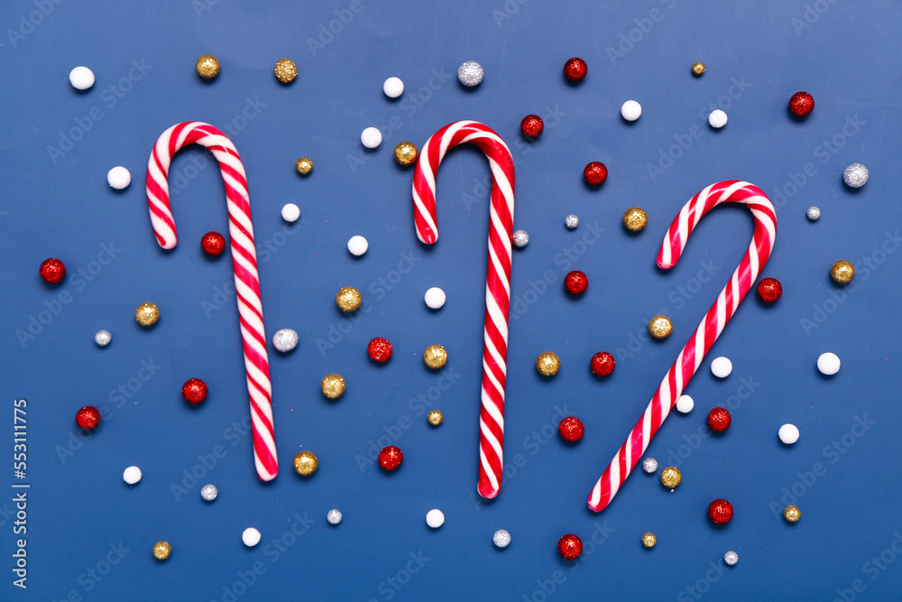 Sweet candy canes and Christmas balls on color background