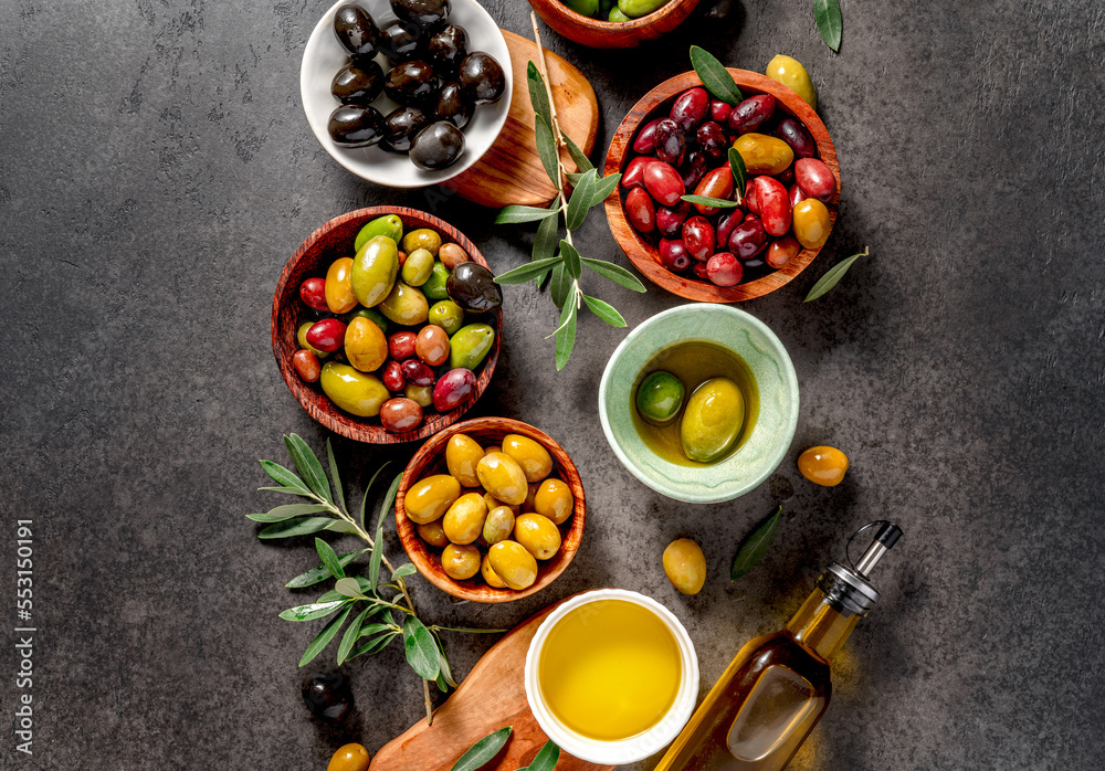 Top view of different olives in bowls on dark background. Olives and bottle of olive. Diet food conc