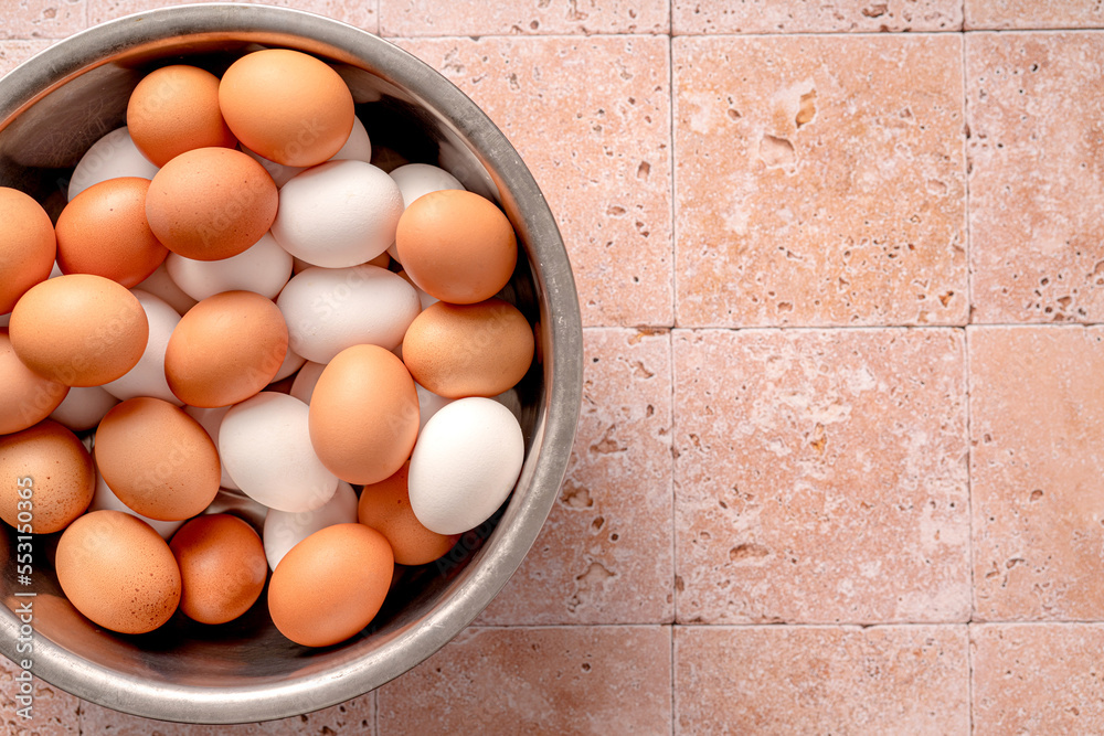 Eggs in metallic bowl on beige background with copy space. Top view of raw brown eggs and white eggs