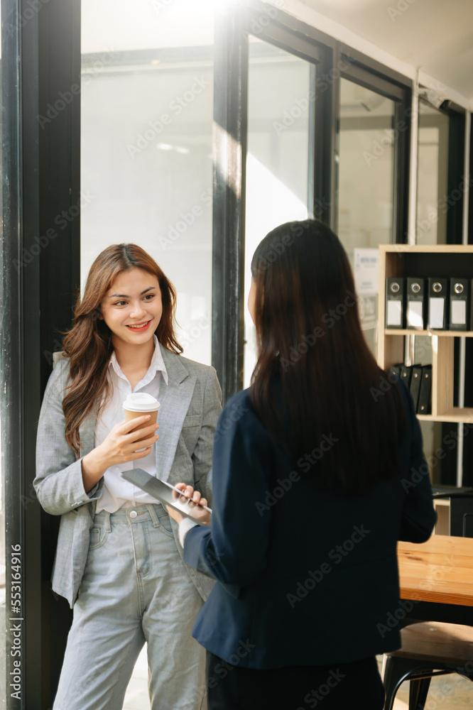 Happy two Asian business woman holding coffee cup in coworking office.