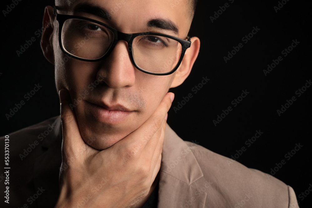 Young Asian man in eyeglasses touching face on black background