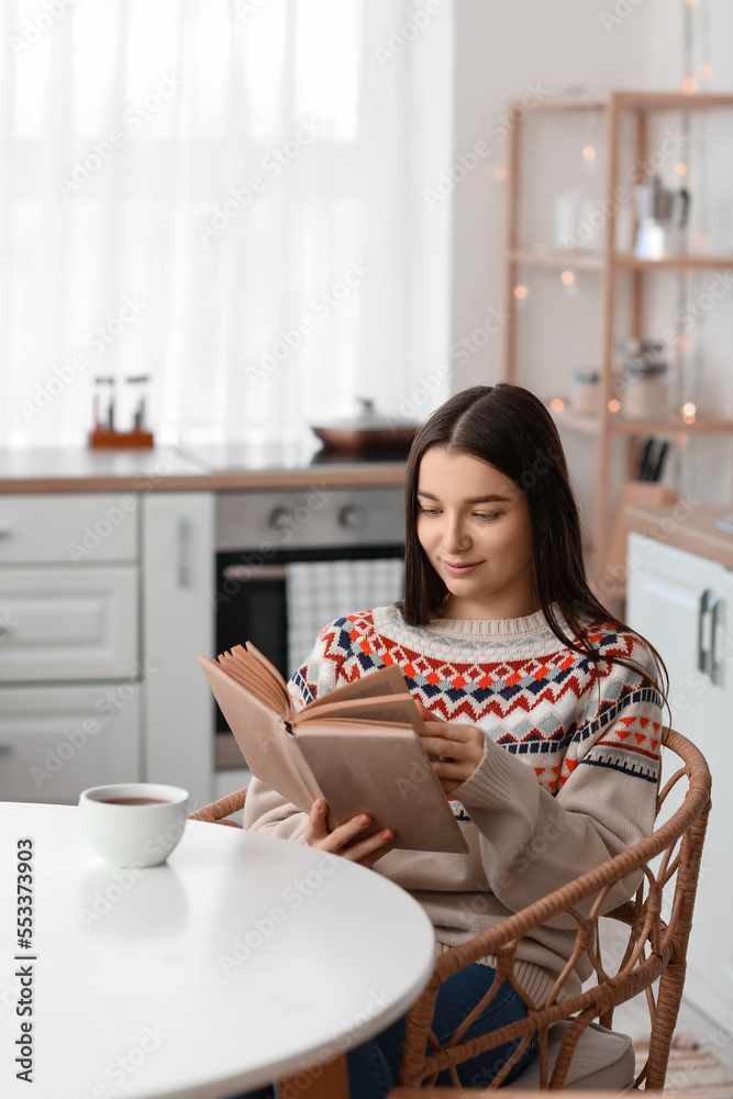 Young woman reading book at dining table in kitchen