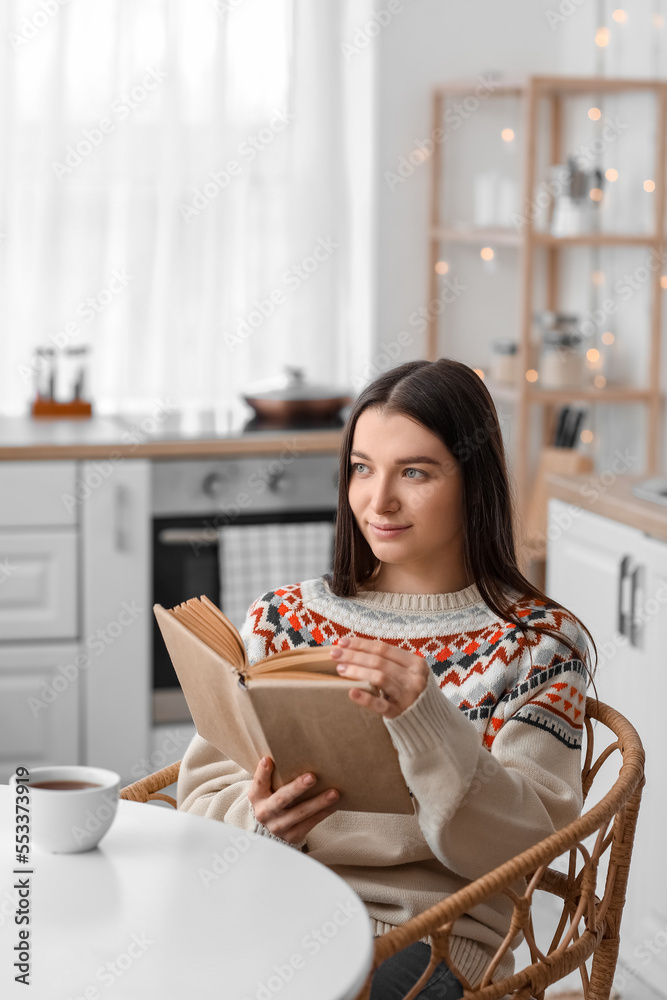 Young woman reading book at dining table in kitchen