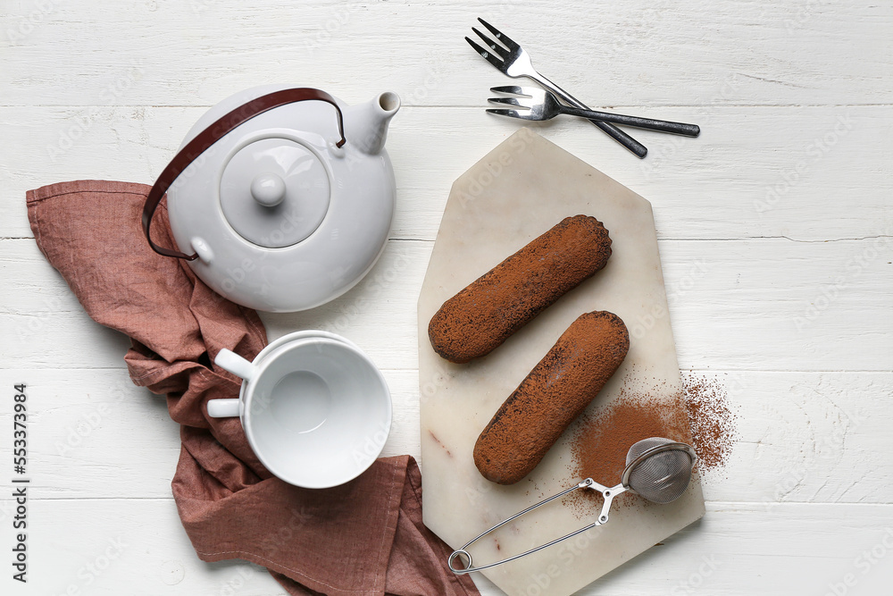 Board with tasty chocolate eclairs and tea set on white wooden background