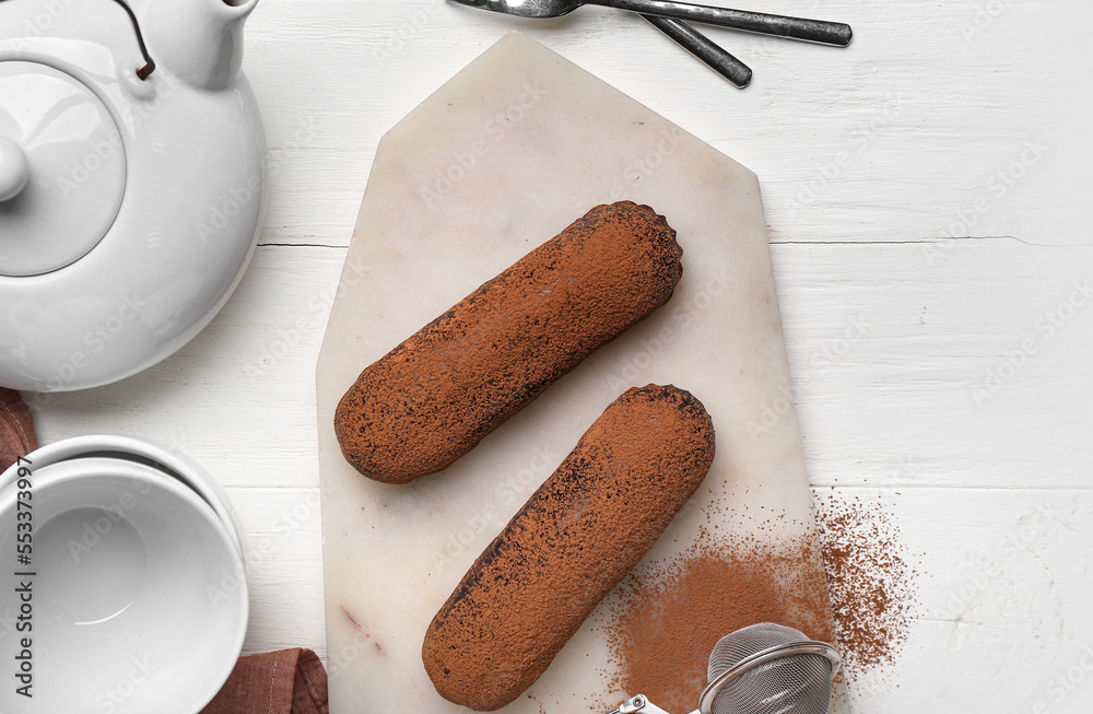 Board with tasty chocolate eclairs and tea set on white wooden background, closeup