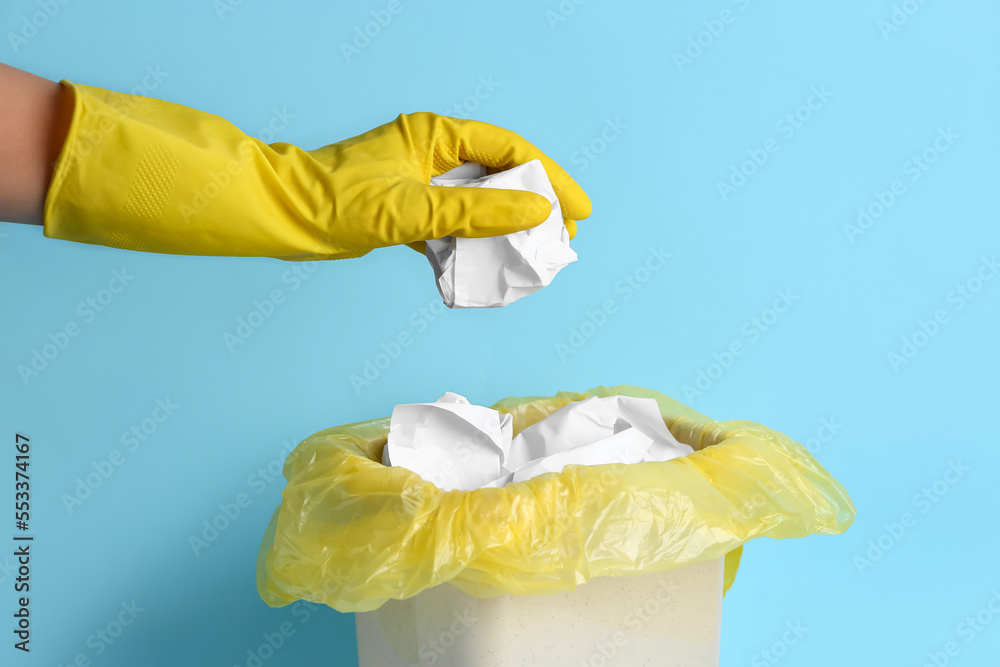 Woman throwing crumpled paper into rubbish bin on color background