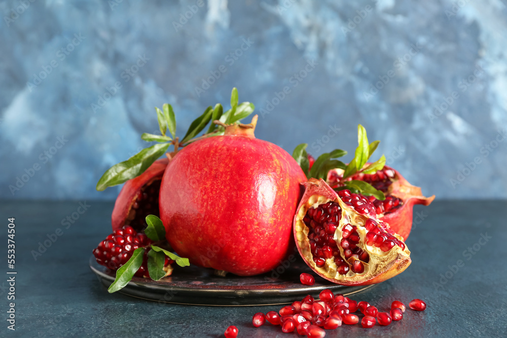 Plate of fresh pomegranates on color background