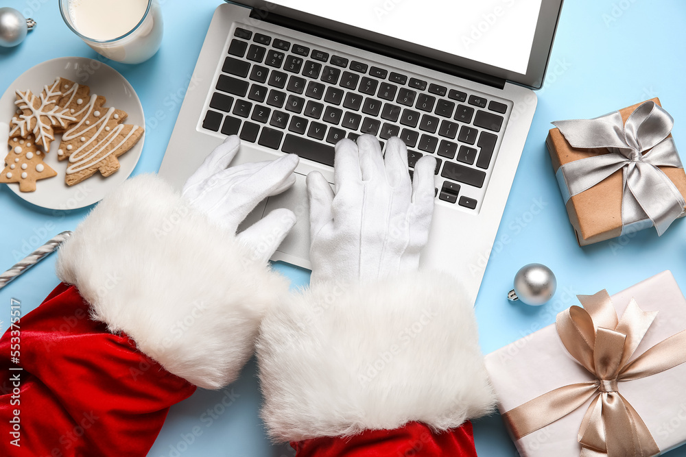 Santa Claus using laptop on blue background, closeup