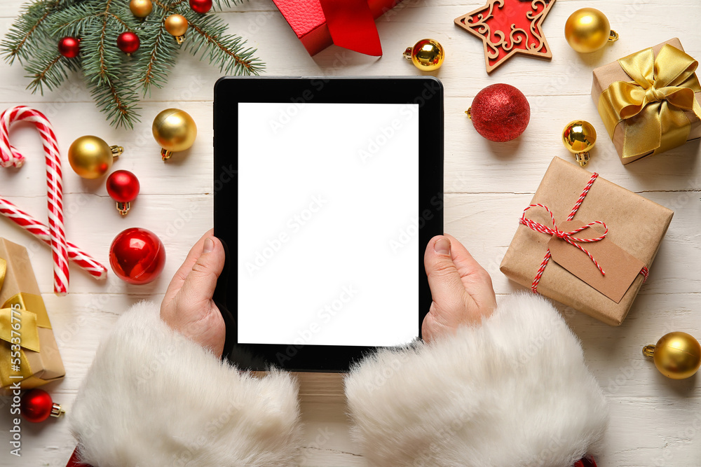 Santa Claus with tablet computer, Christmas decor and gifts on white wooden background