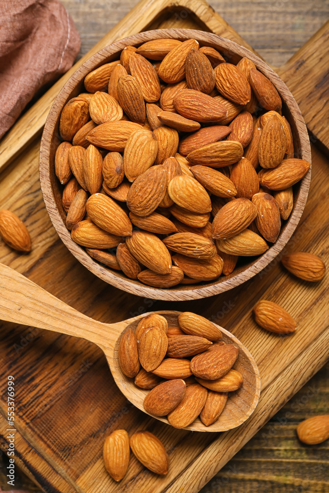 Board with bowl of almonds on wooden background