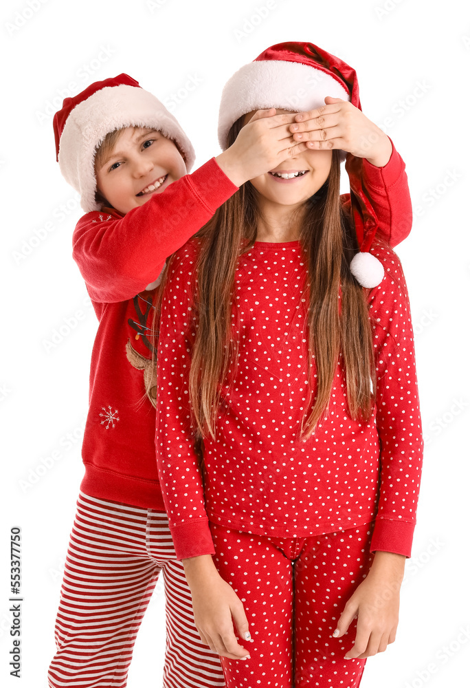 Little boy in Santa hat closing his sisters eyes on white background