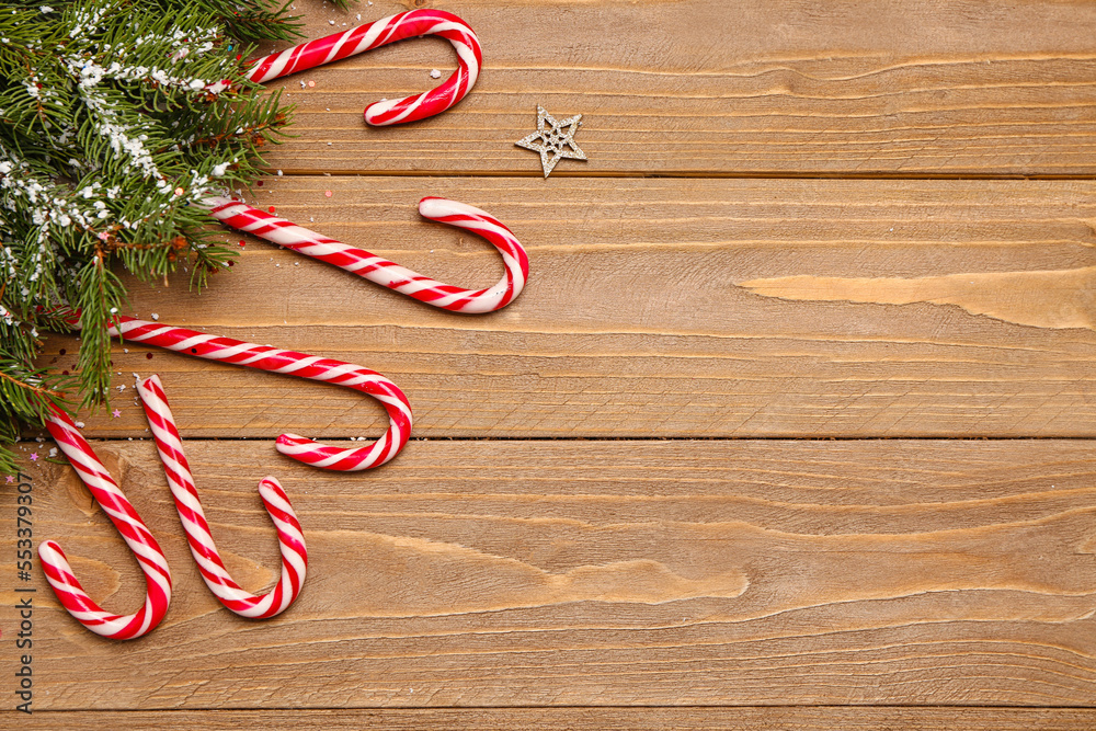 Composition with sweet candy canes and fir branches on wooden background