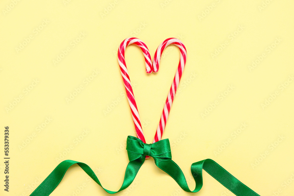 Heart made of sweet candy canes and green ribbon on color background