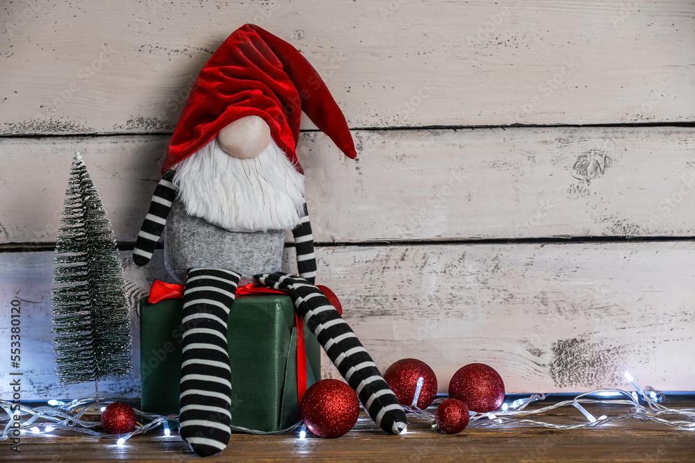 Christmas gnome, gift box, decorations and glowing lights on wooden table