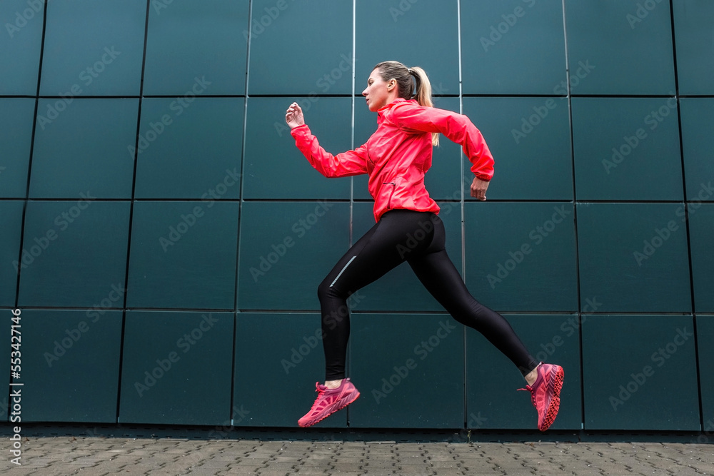 Woman runner, jump on sidewalk on modern background.