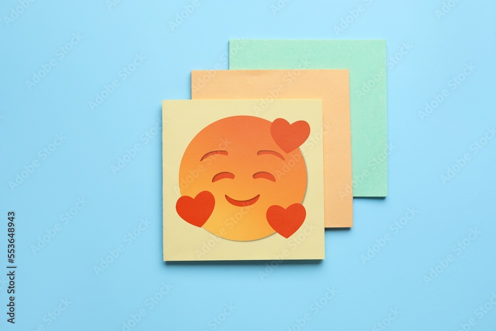 Sticky note with happy emoticon on light blue background