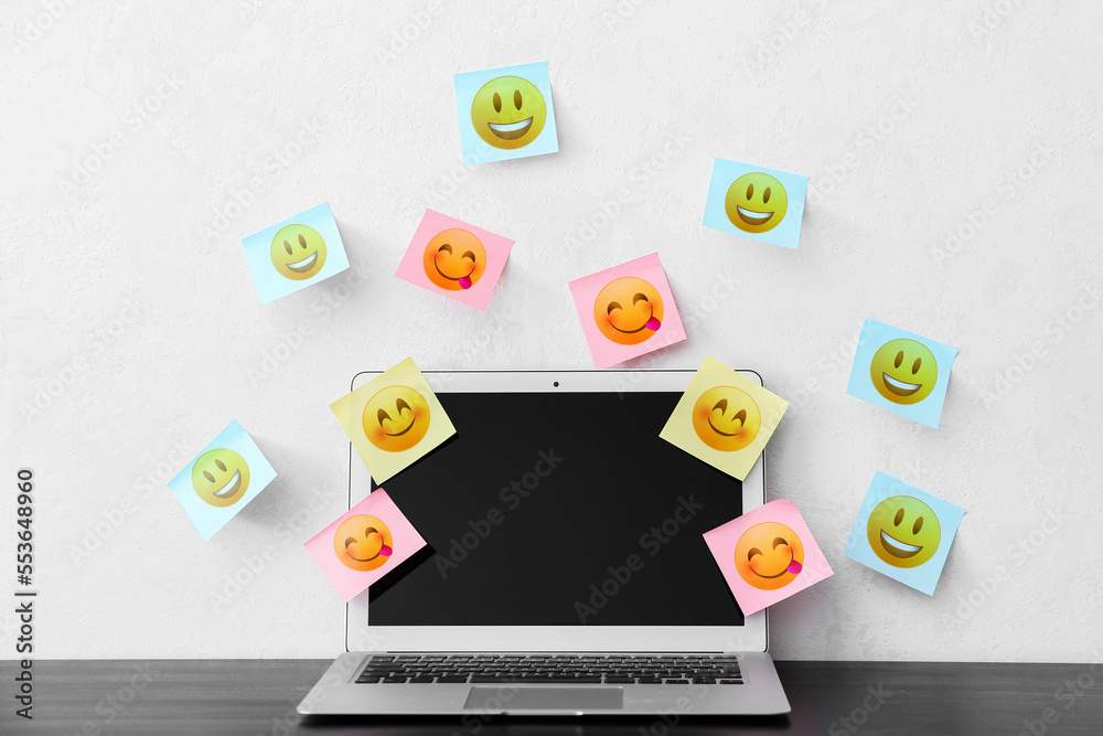 Modern laptop and different sticky note papers with drawn emoticons on light background