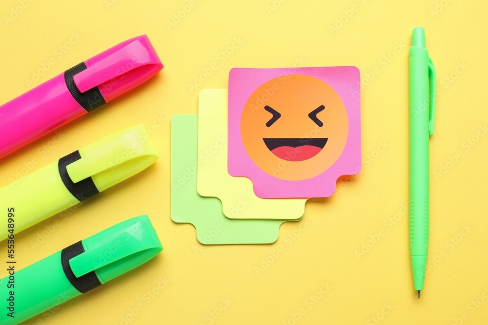 Sticky note with happy emoticon, markers and pen on color background