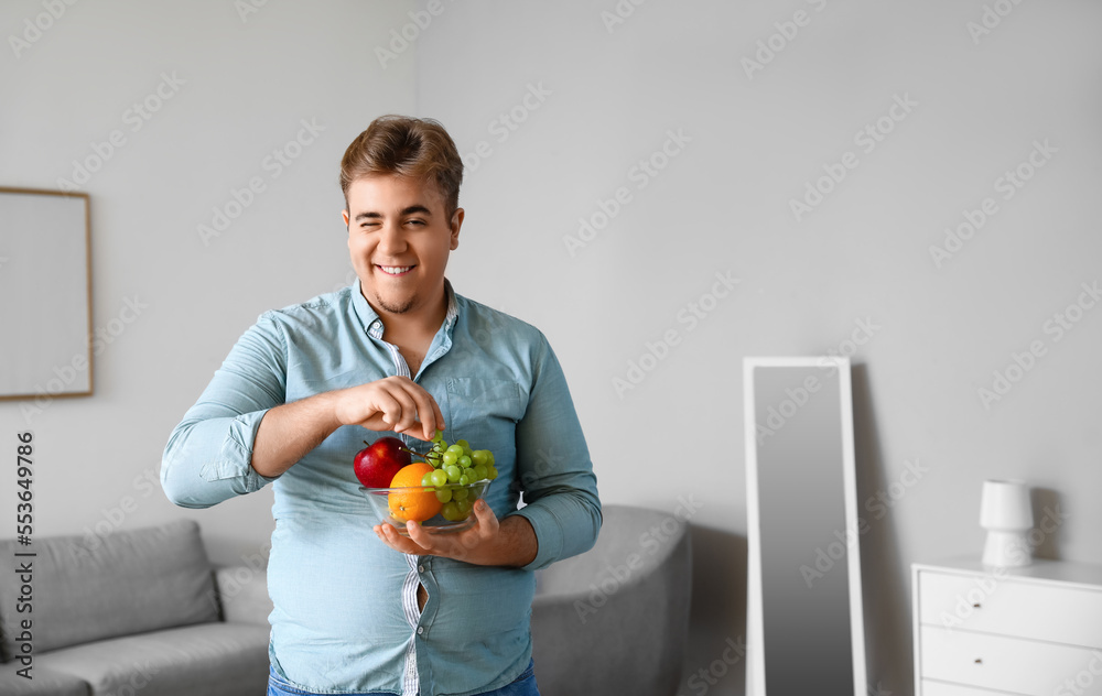 Young overweight man with bowl of fruits at home