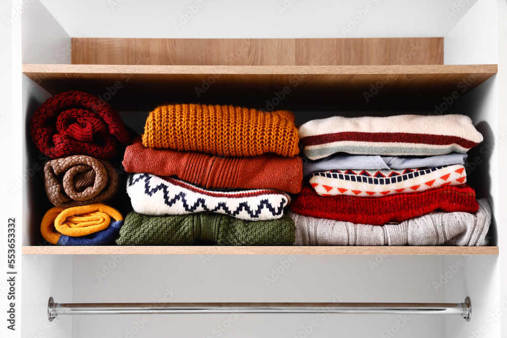 Warm knitted sweaters on shelf in wardrobe, closeup