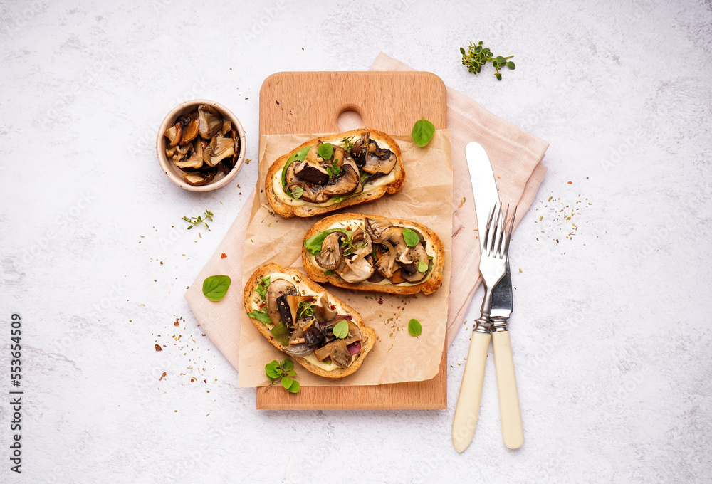 Wooden board of tasty toasts with cream cheese and mushrooms on light background