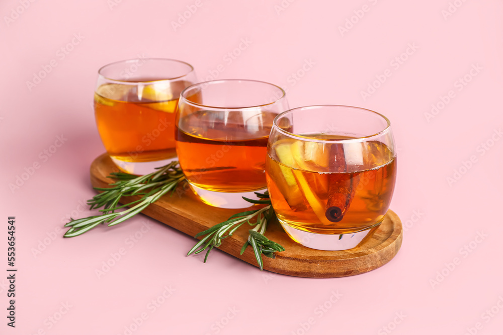 Wooden board with glasses of fresh apple juice and rosemary on pink background