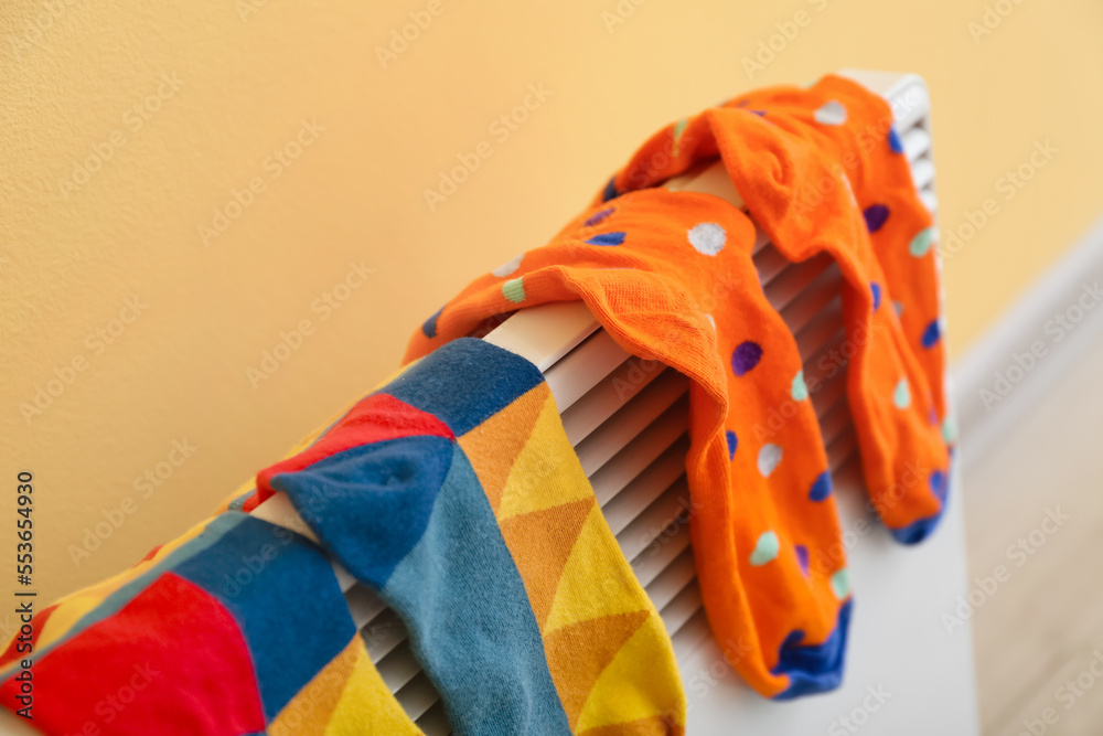 Warm socks drying on electric radiator near yellow wall, closeup