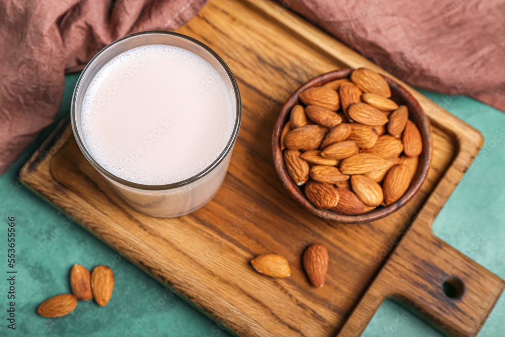 Wooden board with glass of almond milk and nuts on color background, closeup