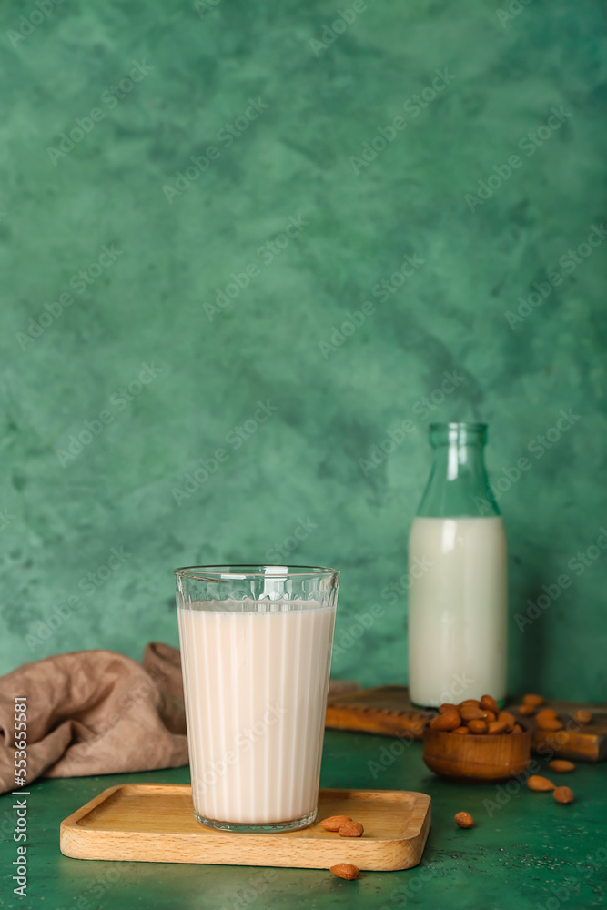 Wooden board with glass of almond milk and nuts on color background