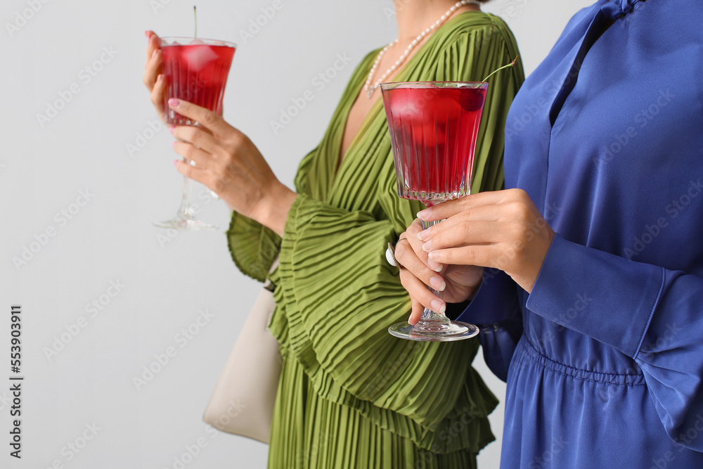 Fashionable women holding glasses with delicious cocktail on light background, closeup