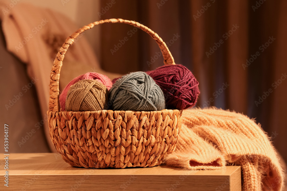 Wicker basket with knitting yarn and clothes on table in room