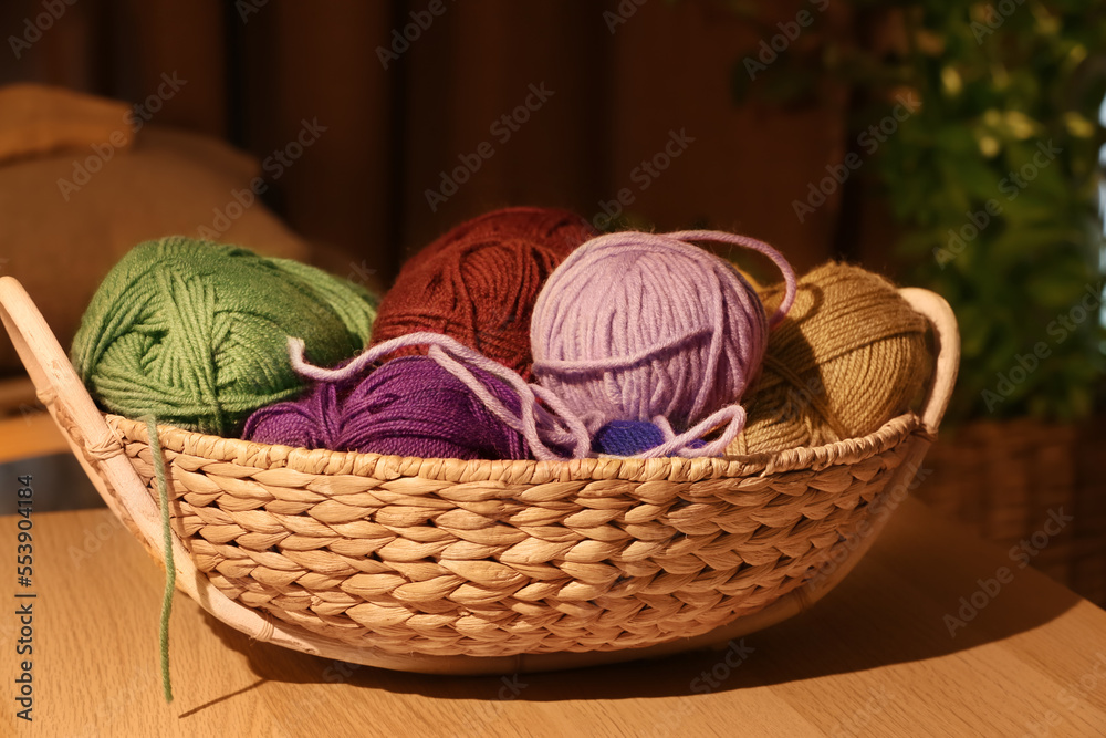 Wicker basket with colorful knitting yarn on table in room