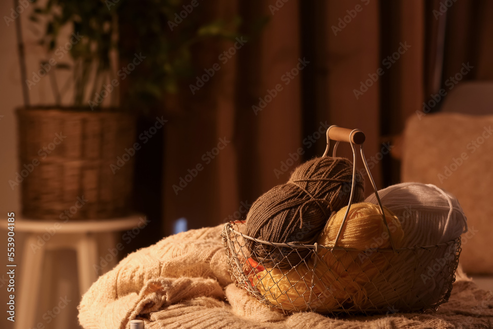 Basket with knitting yarn and clothes on table in room