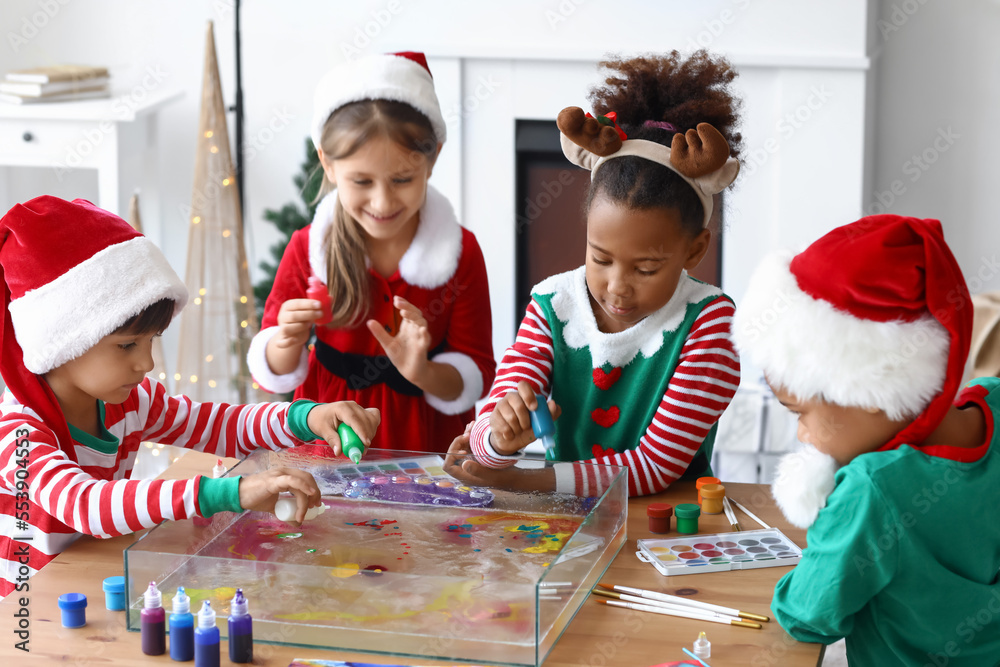 Little children in Christmas costumes pouring paints into water at workshop for Ebru painting