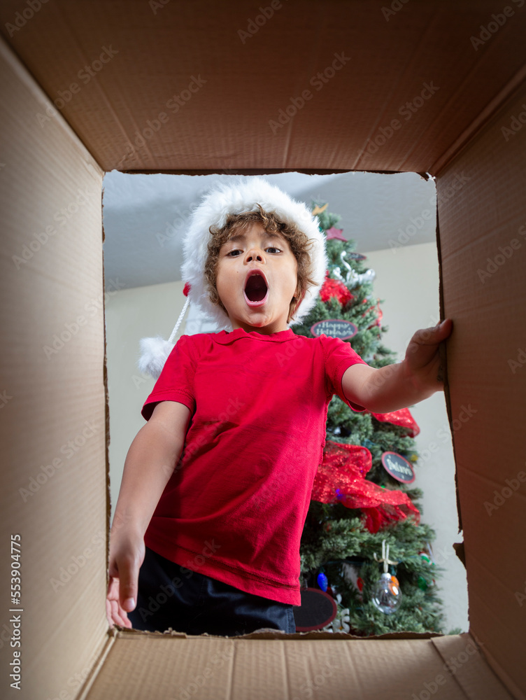 Happy diverse little boy opening a Christmas present on Christmas morning. View from below as he loo