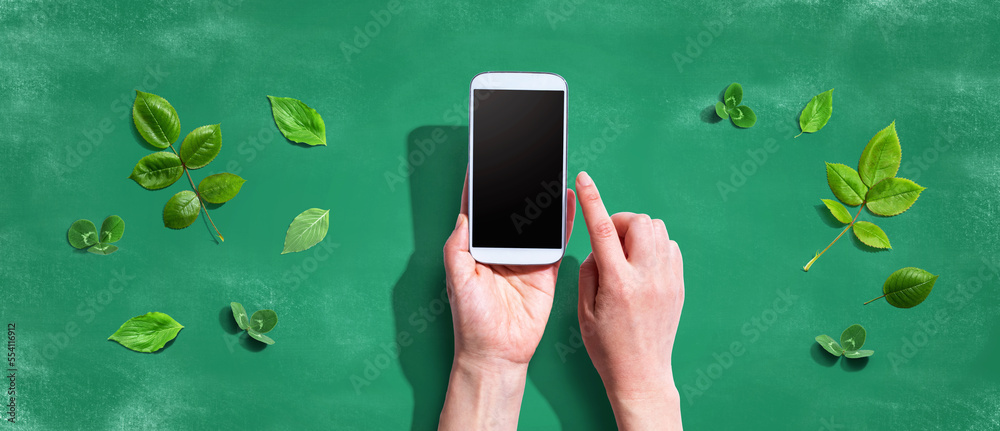 Person using a smartphone with green leaves - flat lay