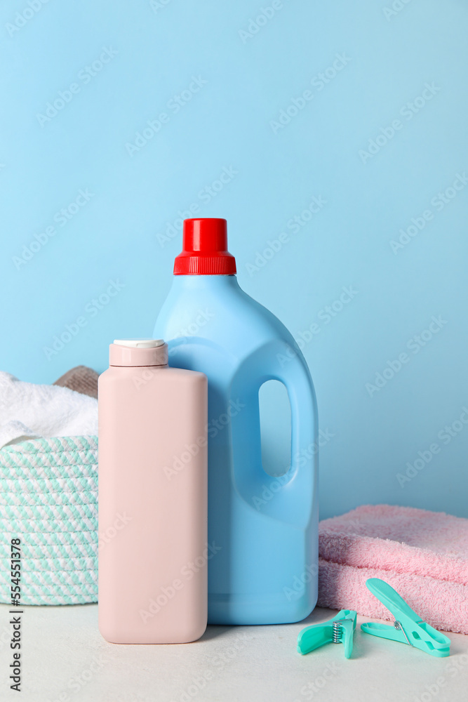 Laundry detergents, towels and basket on table against blue background