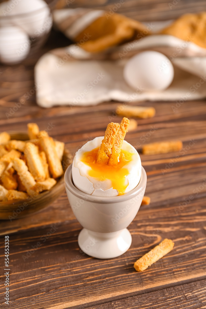 Holder with boiled egg and crunchy croutons on wooden table, closeup