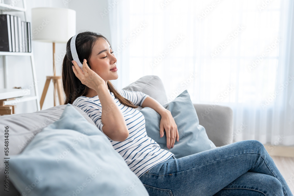 Asian woman listen to music and dancing while sitting on sofa house. 