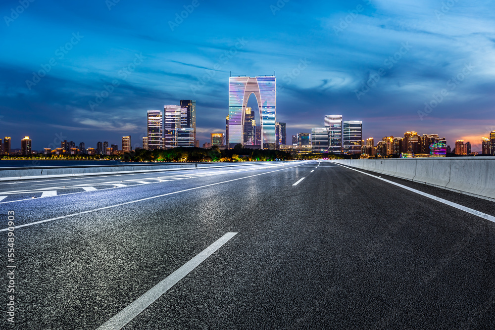 中国苏州的沥青道路和城市天际线，夜晚有现代建筑。