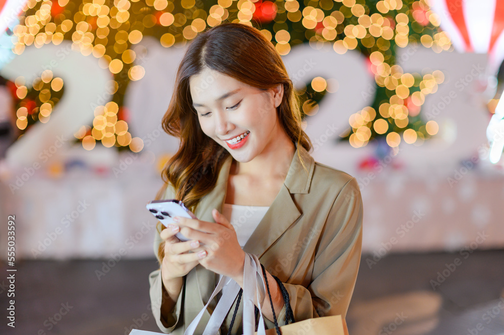 Beautiful asian girl using smartphone shopping online with bags on Christmas tree bokeh light backgr