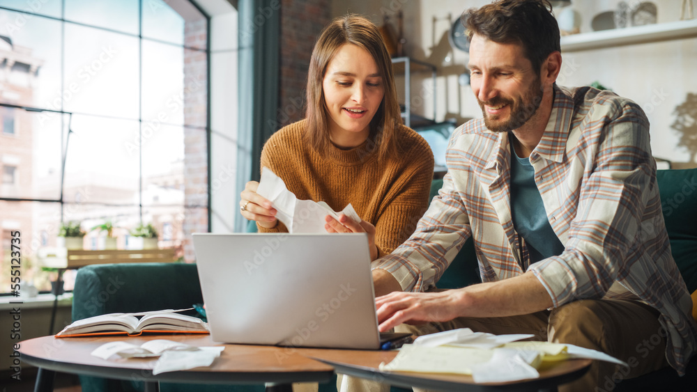 Doing Accounting at Home: Happy Couple Using Laptop Computer, Sitting on Sofa in Apartment. Young Fa