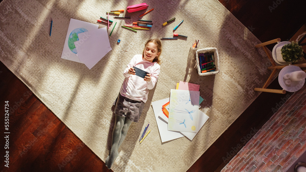 Top View Home: Happy Little Girl Using Smartphone While Lying on the Floor. Joyful Sunny Day and Cle