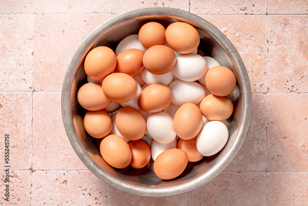 Eggs in metallic bowl on beige background. Top view of raw brown eggs and white eggs with chicken fe