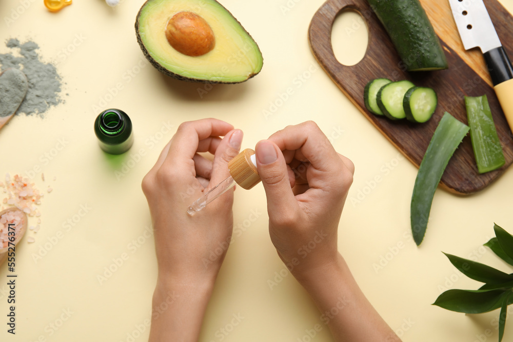 Woman applying essential oil onto hand on color background