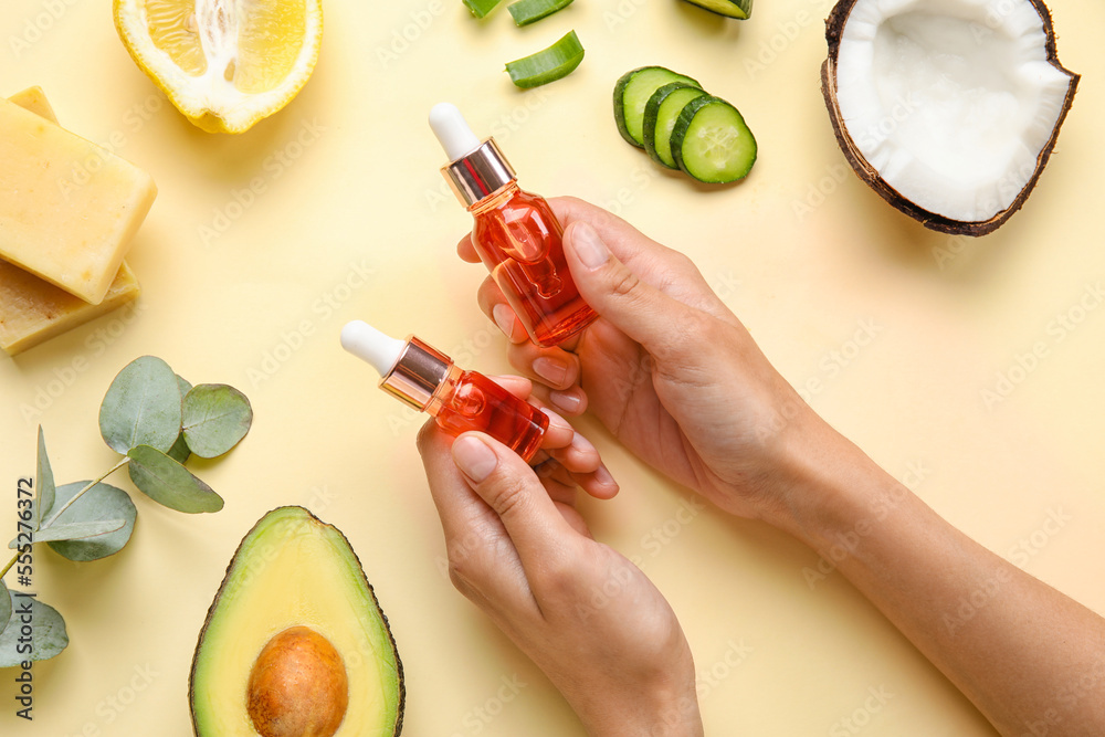 Female hands with bottles of essential oil and ingredients on color background