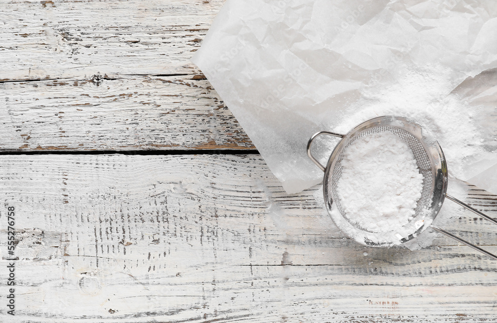 Baking paper and sieve with flour on white wooden background