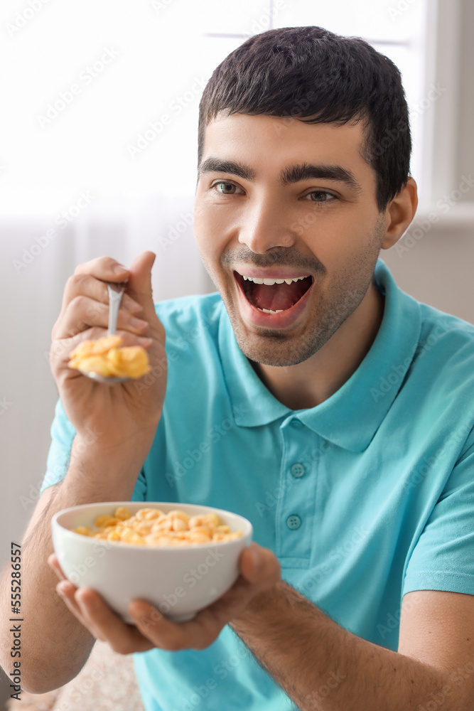 Happy young man eating cornflakes with spoon at home, closeup