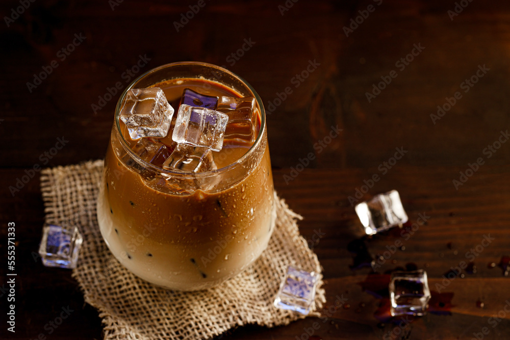 Glass of iced coffee with milk on dark wooden background, top view, copy space. 