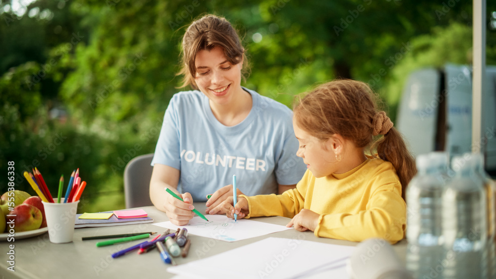 Talented Small Girl in a Yellow Jumper Drawing Beautiful Pictures Together with a Female Volunteer f